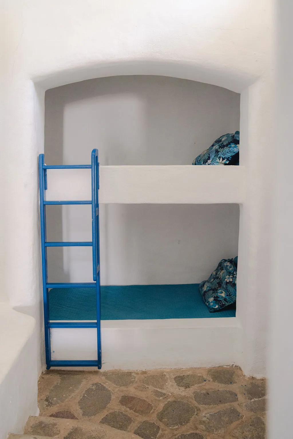 Camarote de obra con escalera azul y piso de piedra.