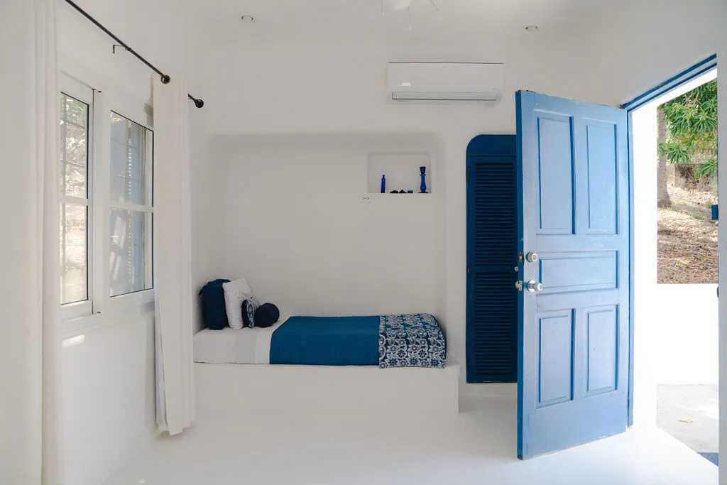 Vista de una cama individual junto a una puerta azul.