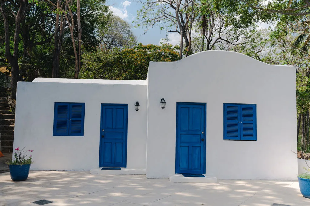 Dos fachadas blancas con puertas y ventanas azules.