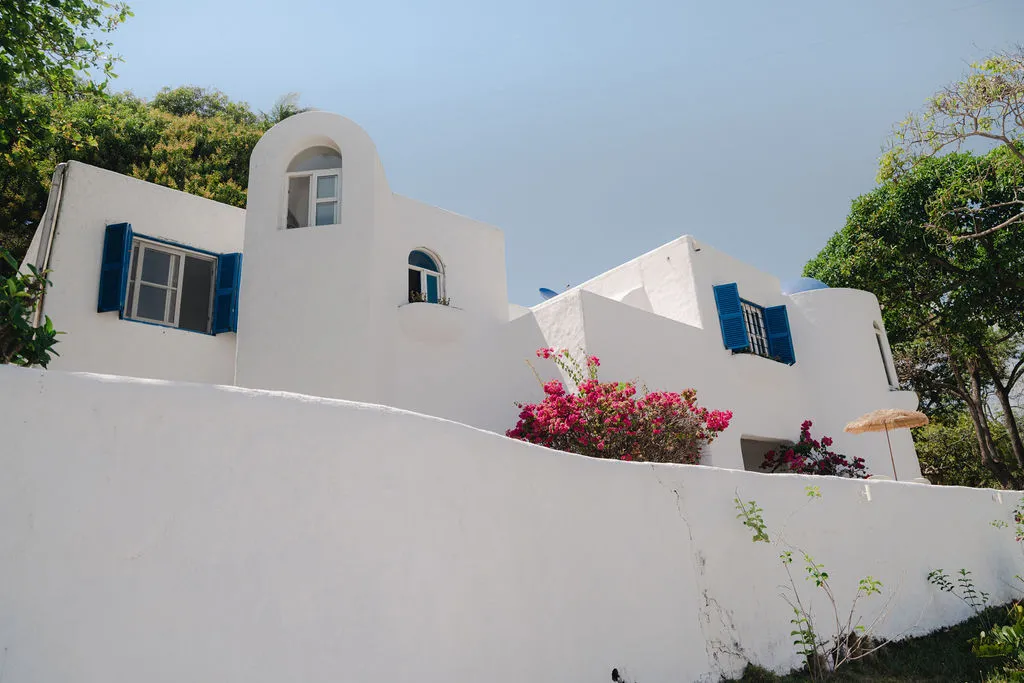 Fachada blanca con ventanas azules y buganvilias.