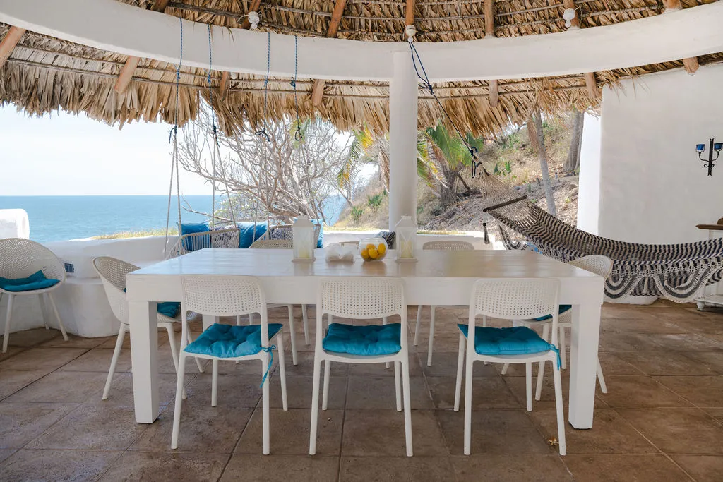 Mesa compartida bajo el rancho, con hamacas y vista al mar.