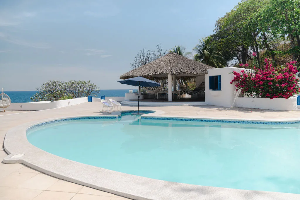 Piscina curva frente al rancho de techo de palma.
